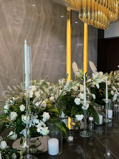 An elegant and modern Diwali tablescape. We used a long arrangement of white flowers and greenery, interspersed with candles of varying heights, set against a dramatic grey marble wall.