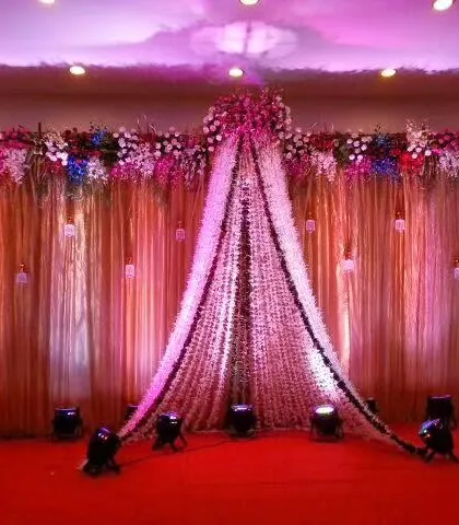 This reception stage features a stunning entrance created with draped pearl strings and flowers. The warm lighting and rich red carpet make for a dramatic and welcoming focal point in the banquet hall.