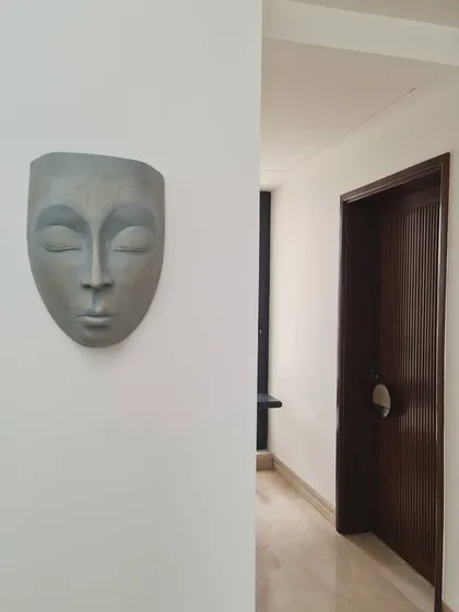 A serene sculptural mask mounted on a clean white wall, adding a touch of contemplative art to a quiet corridor. This snippet from a recently completed residence showcases our love for integrating art into our designs.