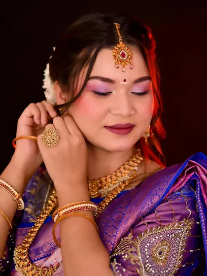 A close-up of a South Indian bride adjusting her earring, showcasing the vibrant eye makeup and traditional gold jewelry.