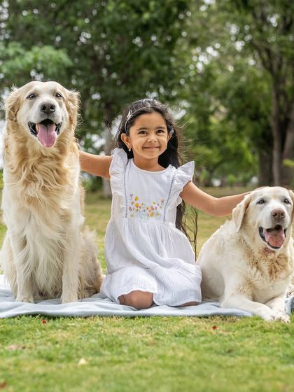 A girl and her two best friends, a Golden Retriever and a senior Labrador. This beautiful outdoor portrait captures her sitting happily between her two loyal companions, showcasing a family full of love for their dogs.