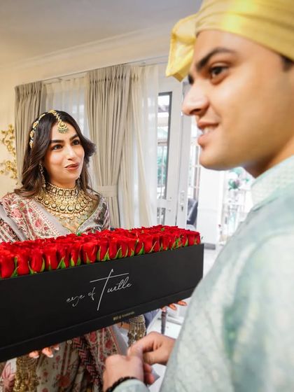 A romantic gesture from the groom, presenting his bride with a box of red roses. Her surprised and happy expression makes this a truly special moment.