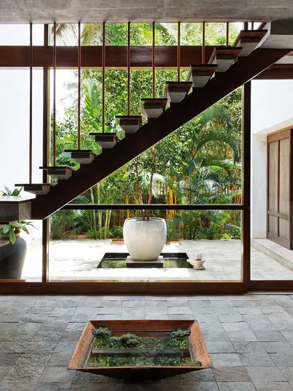 A floating staircase becomes a sculptural element against a wall of glass, dissolving the boundary between the home and the lush tropical garden outside. This design for 'The Tropical House' is a direct expression of our passion for creating homes that live and breathe with nature.