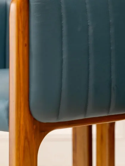 A close-up on the armrest of the accent chair, showing how the rich teakwood frame elegantly wraps around the plush leather upholstery. This is where craftsmanship and comfort meet.