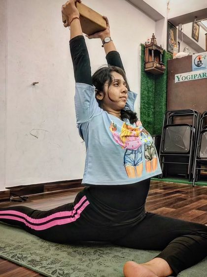 Using a yoga block for support, a student works on her Hanumanasana (splits), improving alignment and depth.