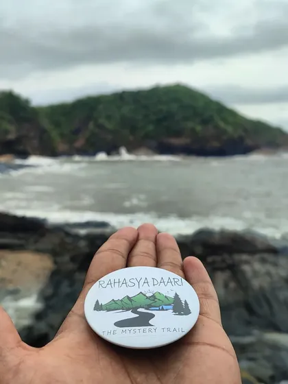 Our badge held up against the backdrop of Om Beach in Gokarna.