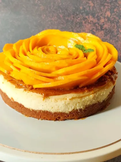 A beautiful and delicious mango cheesecake with a Biscoff crust. The top is decorated with a stunning rose made from thinly sliced Alphonso mangoes.