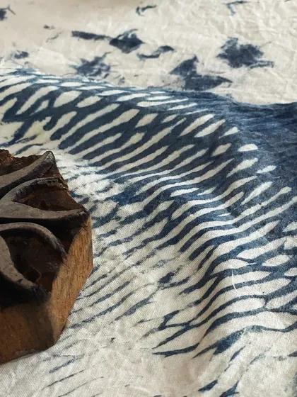 A close-up of a hand-carved wooden block next to a piece of fabric printed with a similar motif. This showcases the traditional tools and beautiful results of block printing with natural indigo.