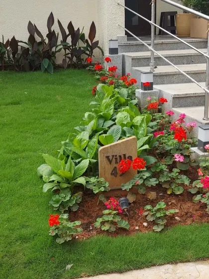 A colorful flower bed with red geraniums and other seasonal flowers adds a splash of vibrancy to this villa's entrance. The wooden sign 'Villa 42' is neatly integrated into the planting scheme.