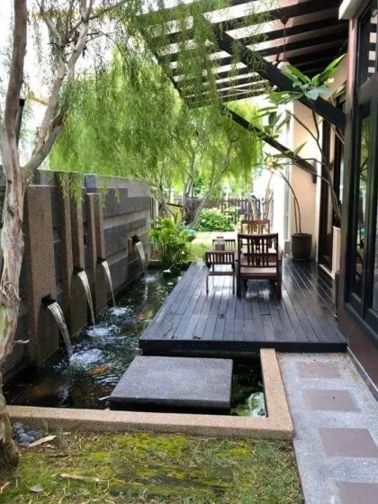 A modern water feature with multiple spouts creating gentle streams into a pond. This design, set against a textured stone wall and surrounded by lush greenery, adds a sophisticated and calming element to the landscape.