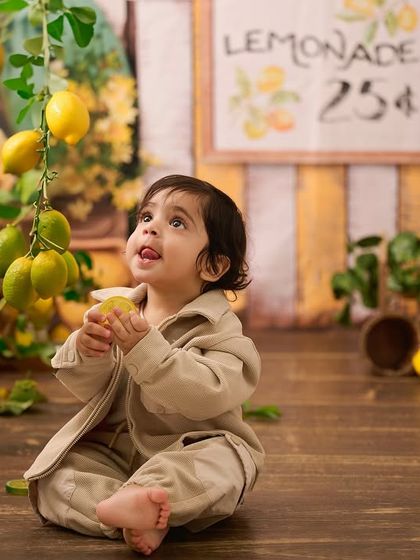 Our lemonade stand setup is full of delightful details. Here, a little one looks up in wonder at the hanging lemons, creating a sweet, candid moment.