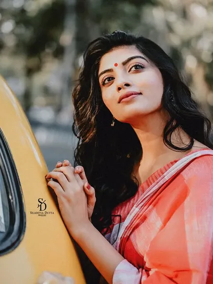 A model leans against a yellow taxi, looking up with a hopeful expression. The warm sunlight and the classic red bindi create a simple yet beautiful portrait.