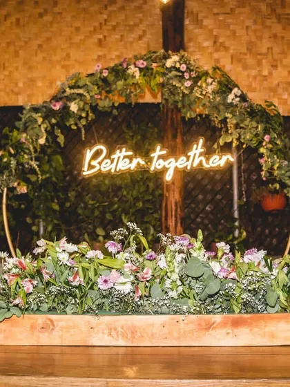 This 'Better Together' neon sign served as the centerpiece for a rustic-themed anniversary backdrop. I combined it with a circular metal arch adorned with lush greenery and wildflowers to create a modern yet natural look for the couple's celebration.