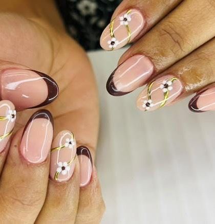 A lovely floral design with a modern twist. This set combines a classic brown French tip with accent nails featuring hand-painted daisies and crisscrossing gold lines.