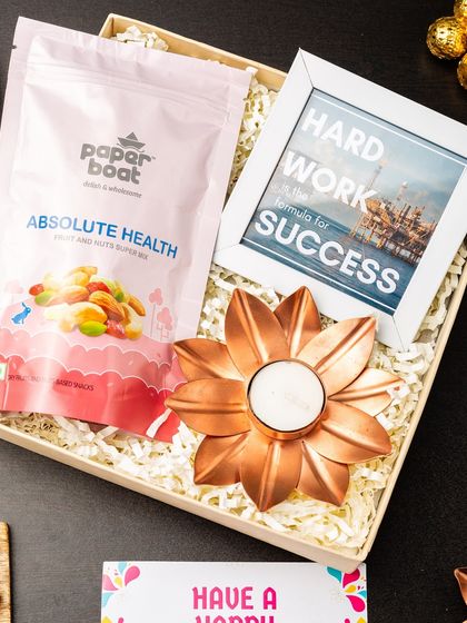 This corporate hamper is designed to motivate and appreciate. It includes a framed motivational quote, a pack of healthy nuts, and a decorative copper diya, perfect for recognizing hard work.