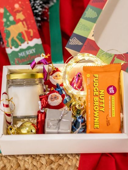 This Christmas hamper is a box of pure festive joy. It contains a jar candle, a nutty fudge brownie, and a variety of cute Christmas tree ornaments and candy canes.