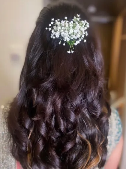 A simple and natural half-updo with soft waves, adorned with fresh baby's breath. This is a perfect look for a bride who wants an understated and elegant style.