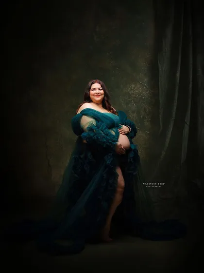A classic portrait of a mother-to-be in a dark green ruffled gown. The painterly, textured backdrop adds depth and an artistic quality to the image.