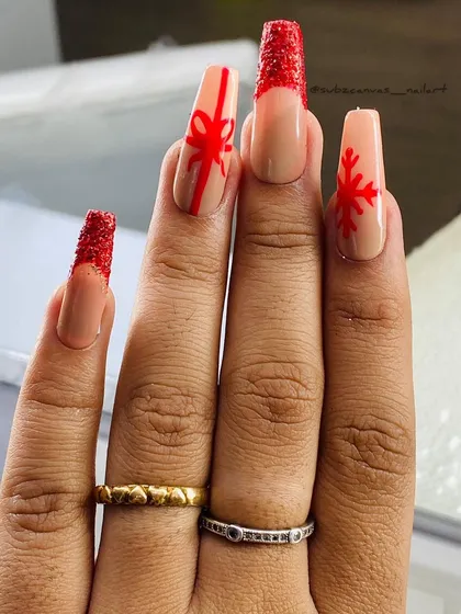 A playful Christmas gift-themed set. These long, square nails feature red glitter tips and hand-painted details like a bow and a snowflake on a nude base.