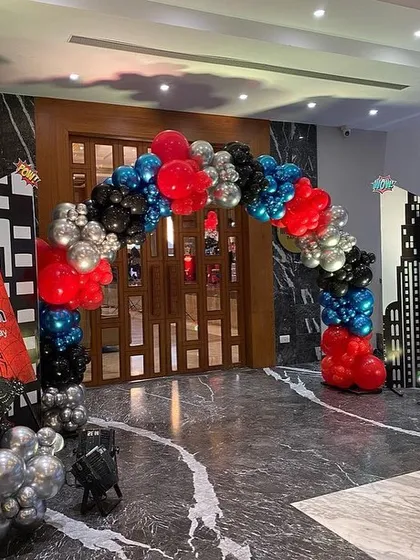 The entrance to an action-packed Spider-Man birthday party, featuring a balloon arch in red, black, and silver, city skyline cutouts, and a personalized welcome sign.