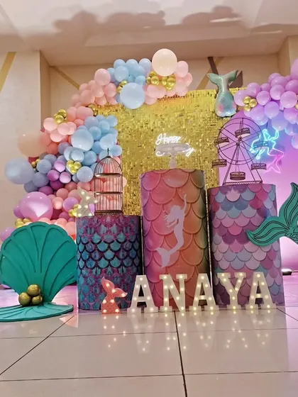 An enchanting mermaid theme for a 6th birthday party. This setup captures the magic of the sea with a shimmering gold backdrop, pastel balloon garlands, mermaid tail cutouts, and a large light-up number '6'.