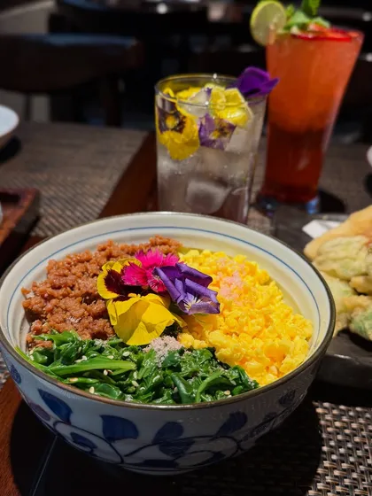 Our Spring Donburi from the Sakura menu. This colorful rice bowl is topped with seasoned ground chicken, fluffy scrambled eggs, and fresh spinach, adorned with edible flowers.