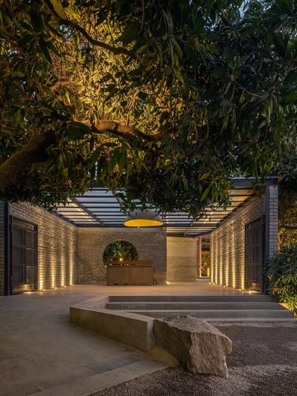 The entrance of a brewery at night, with warm uplighting on the brick walls and surrounding mango trees. The design creates an inviting and sophisticated ambiance from the moment guests arrive.