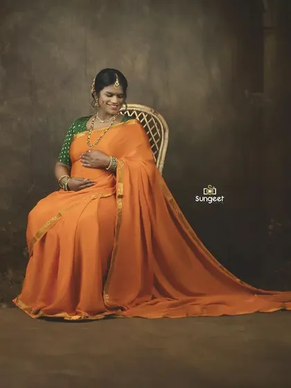 A serene, seated portrait of the mom-to-be in an orange saree. The dark, moody background makes her and the baby bump the central focus.