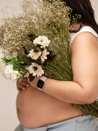 A creative and beautiful close-up. The mother-to-be holds a large bouquet of flowers, partially obscuring her face to draw focus to the baby bump.