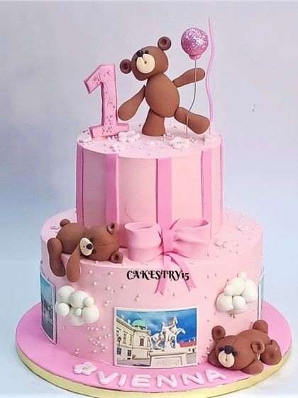 A lovely two-tier pink teddy bear cake for a first birthday. This design features playful teddies, a large pink bow, and edible photos for a personalized touch.