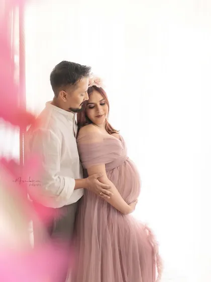 A tender embrace between the couple, framed by soft pink flowers. The high-key lighting and romantic styling make this a beautiful and intimate portrait.