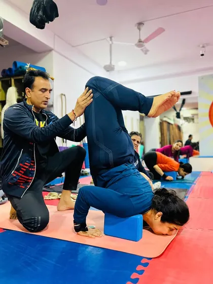 Gentle, hands-on adjustments are key. Here, I am helping a student find the correct alignment and lift in her block-supported forearm stand.