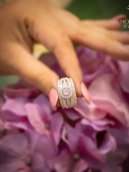 A wide-band diamond ring held delicately over a bouquet of flowers, emphasizing its brilliance and intricate design.
