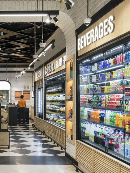 The beverage and chilled sections at Le Marche are clearly demarcated with bold signage. The clean lines of the refrigerators and the continuation of the checkerboard floor create a cohesive and easy-to-navigate retail environment.