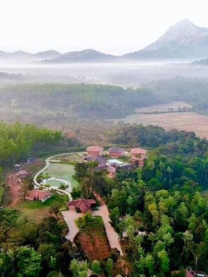An aerial view of a resort in Sakleshpur, surrounded by misty hills and lush paddy fields. It's a hidden gem for a tranquil weekend getaway from Bangalore.