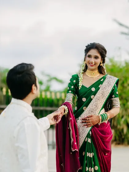 A tender moment as the groom reaches for his bride's hand. Her delighted smile and the gentle gesture create a narrative of love and partnership, captured in a beautiful outdoor setting.