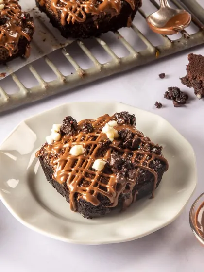 This brownie shot is all about indulgence. The drizzled chocolate and crumbled toppings on a rustic cooling rack create a scene that feels homemade, messy, and incredibly delicious.