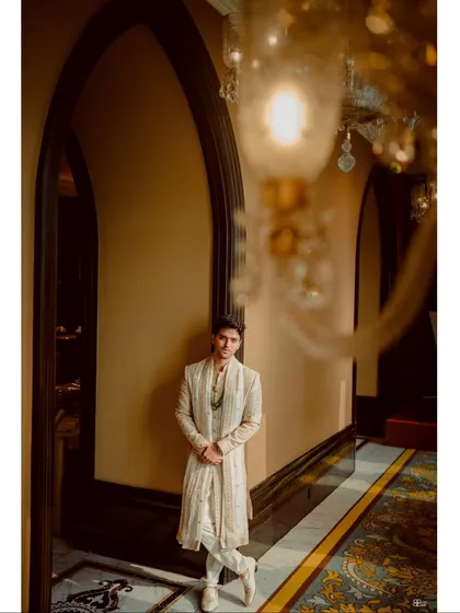 A stylish portrait of the groom in a majestic, arched hallway. The architecture and lighting create a sense of grandeur and sophistication.