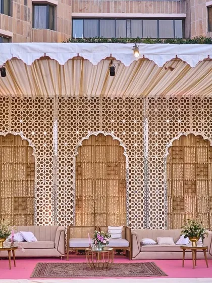 The grand lounge structure with its intricate jali backdrop and scalloped canopy, providing a luxurious and shaded seating area for the outdoor event.
