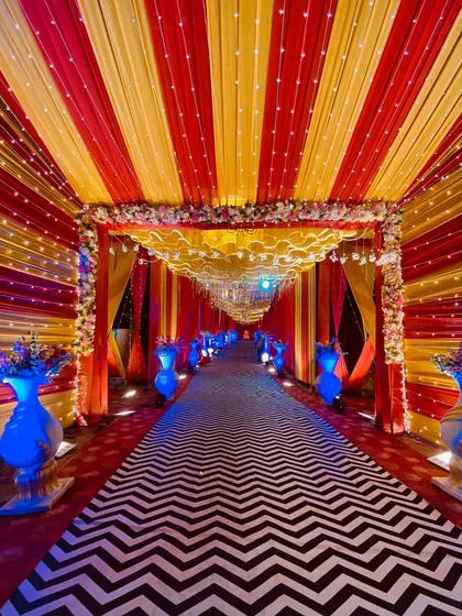 This vibrant entrance combines red and yellow ceiling drapes with a bold chevron carpet. The blue-lit vases provide a cool color contrast.