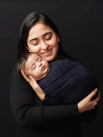 A mother holds her sleeping baby, a gentle smile on her face. The dark, simple background ensures that the focus remains entirely on this beautiful bond.
