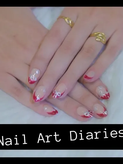 A playful and festive nail art design. This look features a French manicure style with red tips and delicate, hand-painted white bows with a touch of glitter.