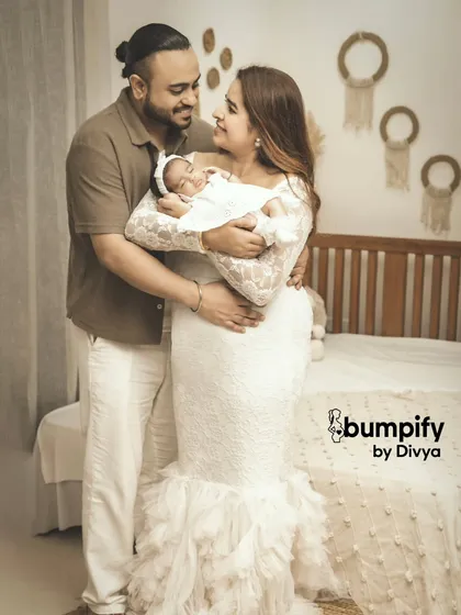 A beautiful family portrait celebrating their new arrival. The parents are dressed in white, creating a soft, serene atmosphere in this newborn studio session.
