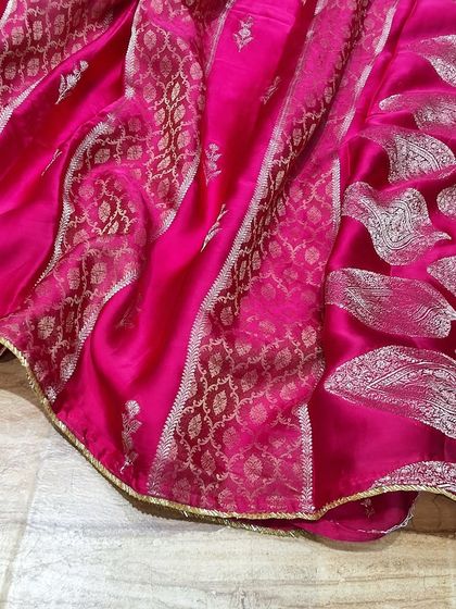A vibrant pink soft silk saree with beautiful silver zari work. The combination of paisley motifs and geometric patterns makes it a standout piece from our festive collection.