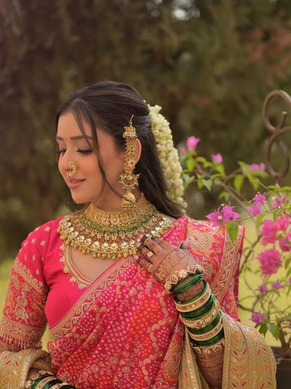 A serene portrait of the bride. The soft lighting highlights her dewy makeup and the intricate details of her pink bandhani saree and traditional jewelry.