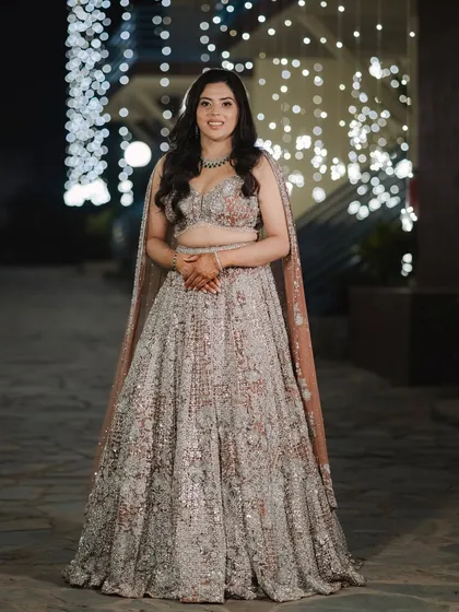 A full-length portrait of the bride, Mehak, at her sangeet. Her sparkling silver and blush lehenga looks stunning against the backdrop of fairy lights.