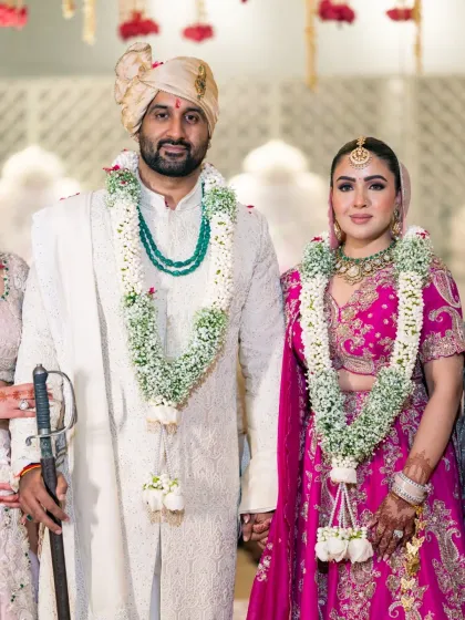 A classic posed portrait of the newly married couple. This photo highlights their coordinated outfits, the beautiful floral garlands, and their connection.