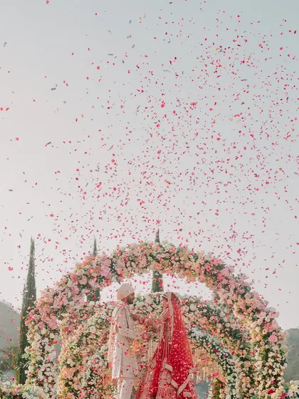 The Varmala is a pinnacle moment, and I ensure it's as beautiful as the love it represents. Here, a shower of delicate rose petals rains down as the couple exchanges garlands under a magnificent floral arch, creating a picture-perfect memory.