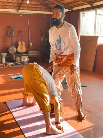I believe in guiding each student personally. Here, I am offering a gentle adjustment in a forward fold, helping the student to find space and release tension safely. My approach is to meet you where you are, with patience and support, so you can trust your body and deepen your practice without force.