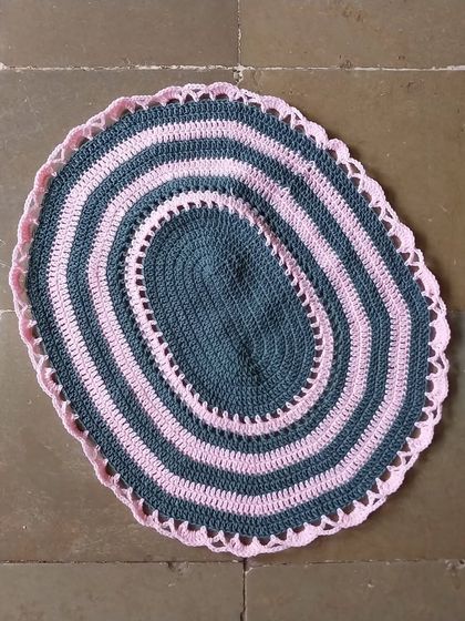 An oval-shaped striped table mat in grey and pink.